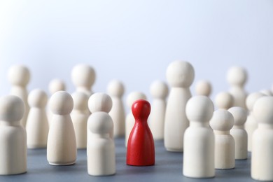 Photo of Human resources concept. Red figure among wooden ones on table against light background, closeup. Space for text