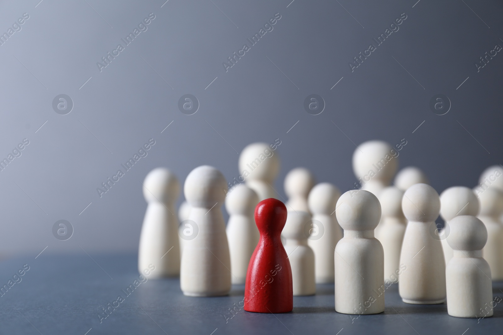 Photo of Human resources concept. Red figure among wooden ones on grey background, closeup. Space for text