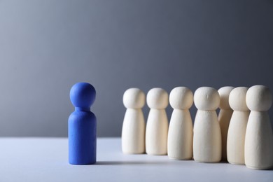 Photo of Human resources concept. Blue figure in front of wooden ones on table against grey background, closeup. Space for text