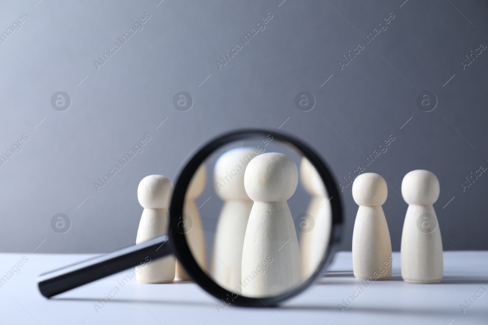 Photo of Human resources concept. Looking at wooden figures through magnifying glass on table against light background, closeup. Space for text