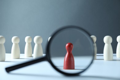 Photo of Human resources concept. Looking at red figure through magnifying glass on table against grey background, closeup