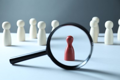 Photo of Human resources concept. Looking at red figure through magnifying glass on table against grey background, closeup