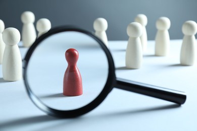 Photo of Human resources concept. Looking at red figure through magnifying glass on table against grey background, closeup