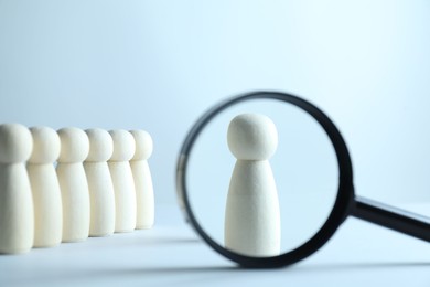 Photo of Human resources concept. Looking at wooden figure through magnifying glass on light background, closeup