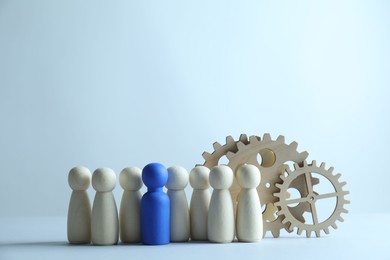 Photo of Human resources concept. Blue figure among wooden ones and gearwheels on light background, closeup. Space for text