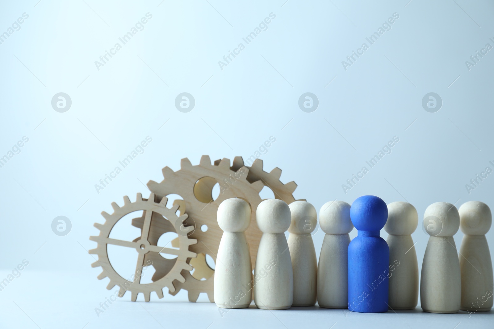 Photo of Human resources concept. Blue figure among wooden ones and gearwheels on light background, closeup. Space for text