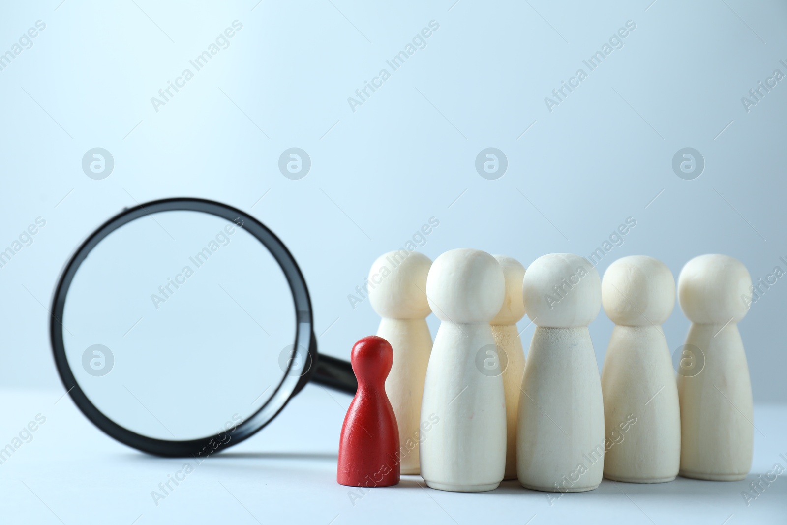 Photo of Human resources concept. Red figure in front of wooden ones and magnifying glass on light background, closeup. Space for text