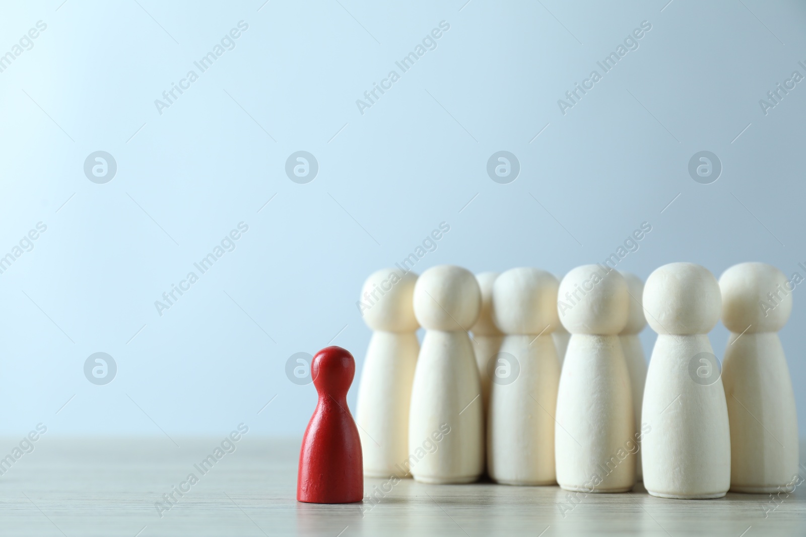 Photo of Human resources concept. Red figure in front of wooden ones on table against light background, closeup. Space for text