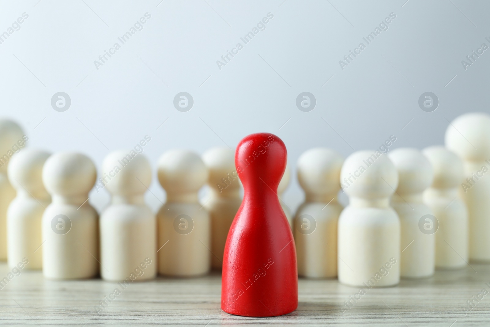 Photo of Human resources concept. Red figure in front of wooden ones on table against light background, closeup