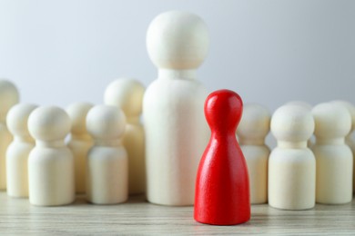 Human resources concept. Red figure in front of wooden ones on table against light background, closeup