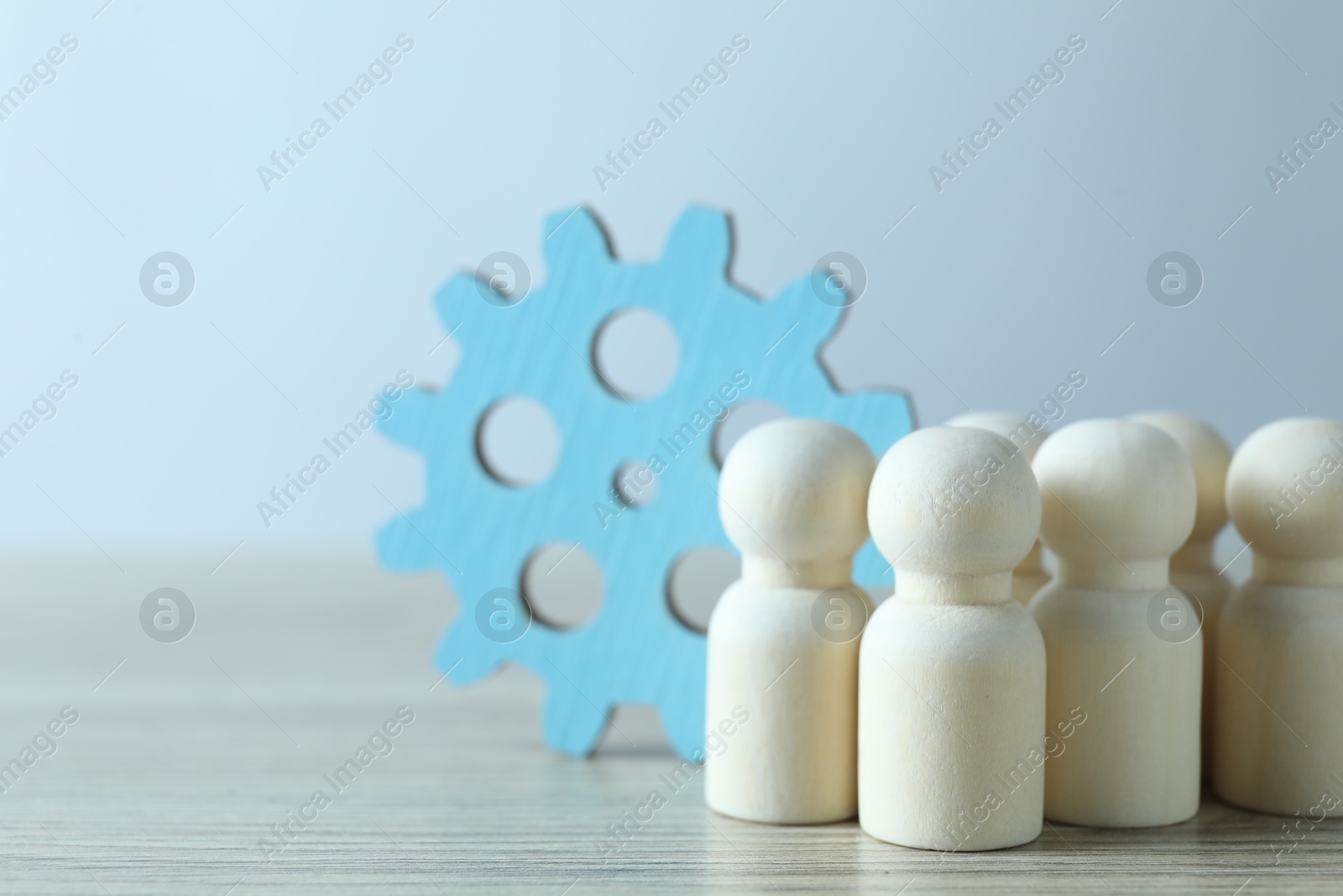 Photo of Human resources concept. Many wooden figures and gearwheel on table against light background, closeup