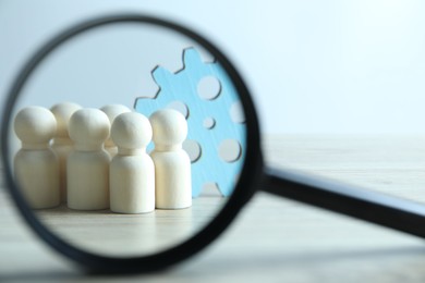 Photo of Human resources concept. Looking at wooden figures and gearwheel through magnifying glass on table against light background, closeup