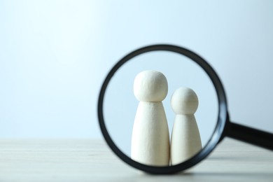 Photo of Human resources concept. Looking at wooden figures through magnifying glass on table against light background, closeup. Space for text