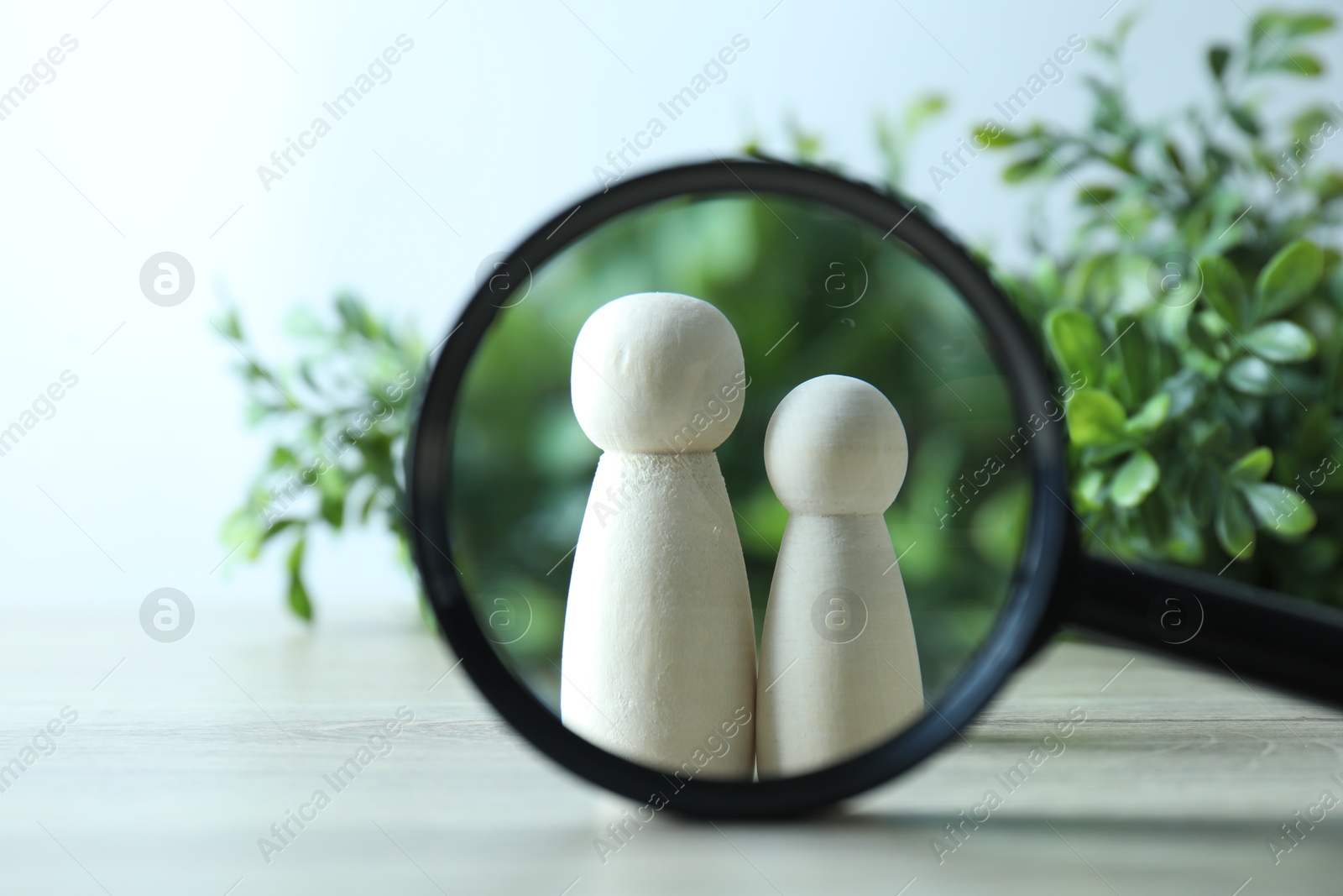 Photo of Human resources concept. Looking at wooden figures through magnifying glass on table against blurred background, closeup