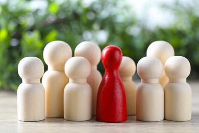 Photo of Human resources concept. Red figure among wooden ones on table against blurred background, closeup