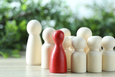 Photo of Human resources concept. Red figure among wooden ones on table against blurred background, closeup