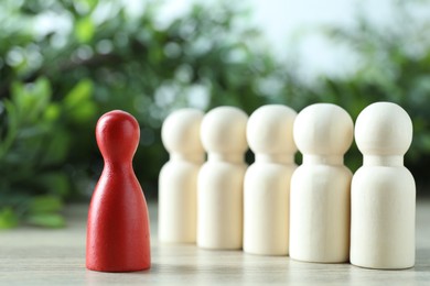 Photo of Human resources concept. Red figure in front of wooden ones on table against blurred background, closeup