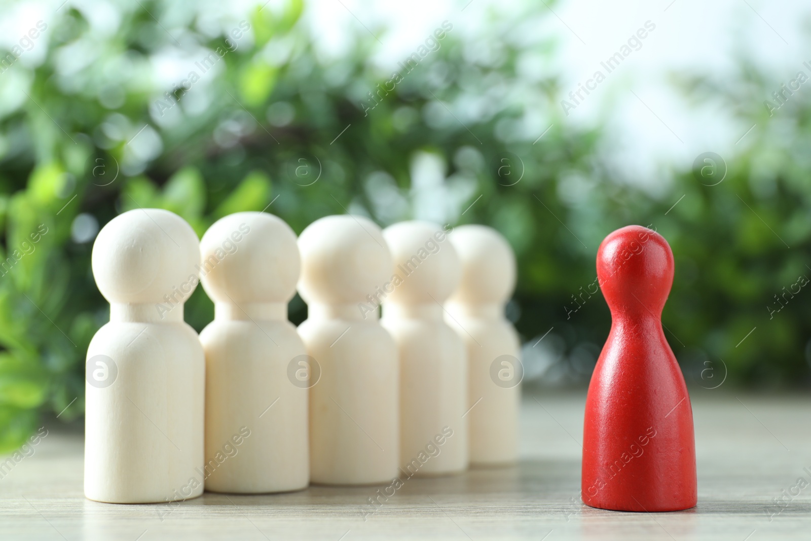 Photo of Human resources concept. Red figure in front of wooden ones on table against blurred background, closeup