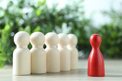 Photo of Human resources concept. Red figure in front of wooden ones on table against blurred background, closeup