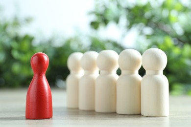 Photo of Human resources concept. Red figure in front of wooden ones on table against blurred background, closeup