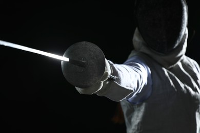 Photo of Fencer with epee on black background, selective focus