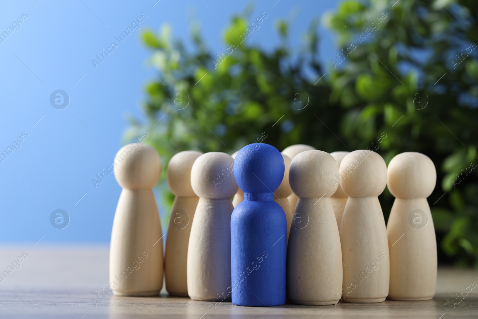 Photo of Human resources concept. Blue figure among wooden ones on table against blurred background, closeup. Space for text