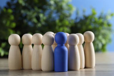 Photo of Human resources concept. Blue figure among wooden ones on table against blurred background, closeup. Space for text