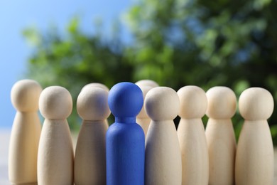 Photo of Human resources concept. Blue figure among wooden ones on table against blurred background, closeup. Space for text