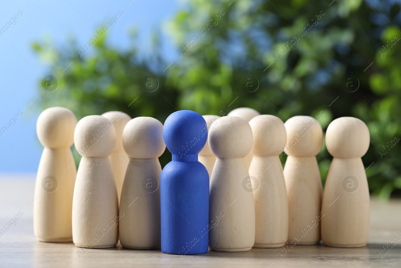 Photo of Human resources concept. Blue figure among wooden ones on table against blurred background, closeup. Space for text