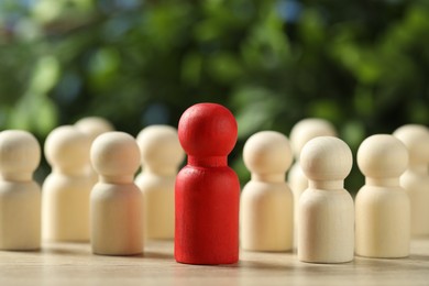 Photo of Human resources concept. Red figure in front of wooden ones on table against blurred background, closeup. Space for text