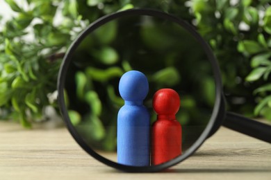 Photo of Human resources concept. Looking at color figures through magnifying glass on wooden table against blurred background, closeup