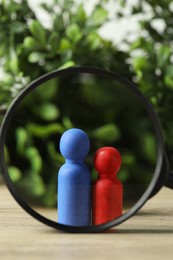 Photo of Human resources concept. Looking at color figures through magnifying glass on wooden table against blurred background, closeup