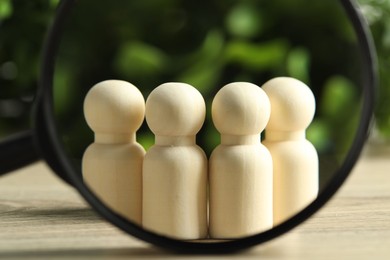 Photo of Human resources concept. Looking at wooden figures through magnifying glass on table against blurred background, closeup