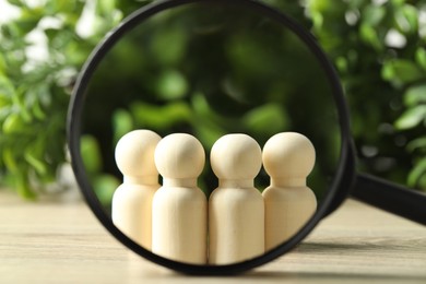 Photo of Human resources concept. Looking at wooden figures through magnifying glass on table against blurred background, closeup