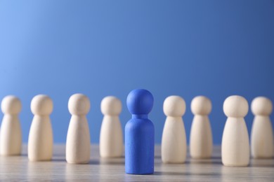 Photo of Human resources concept. Blue figure in front of wooden ones on table, closeup. Space for text