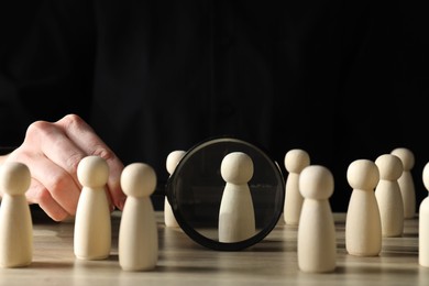 Photo of Human resources concept. Woman with magnifying glass and wooden pieces at table, closeup