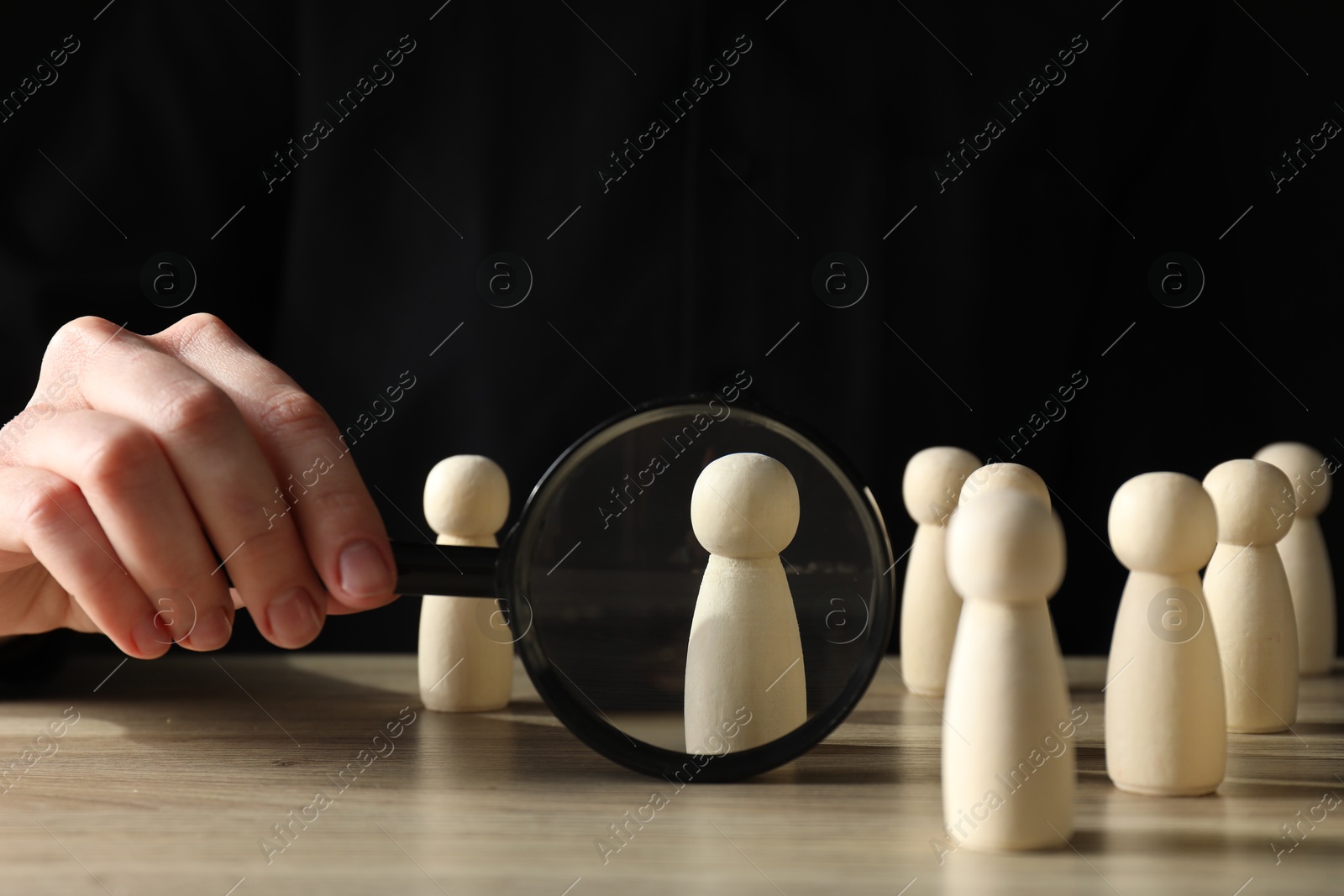 Photo of Human resources concept. Woman with magnifying glass and wooden pieces at table, closeup