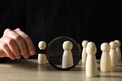 Photo of Human resources concept. Woman with magnifying glass and wooden pieces at table, closeup