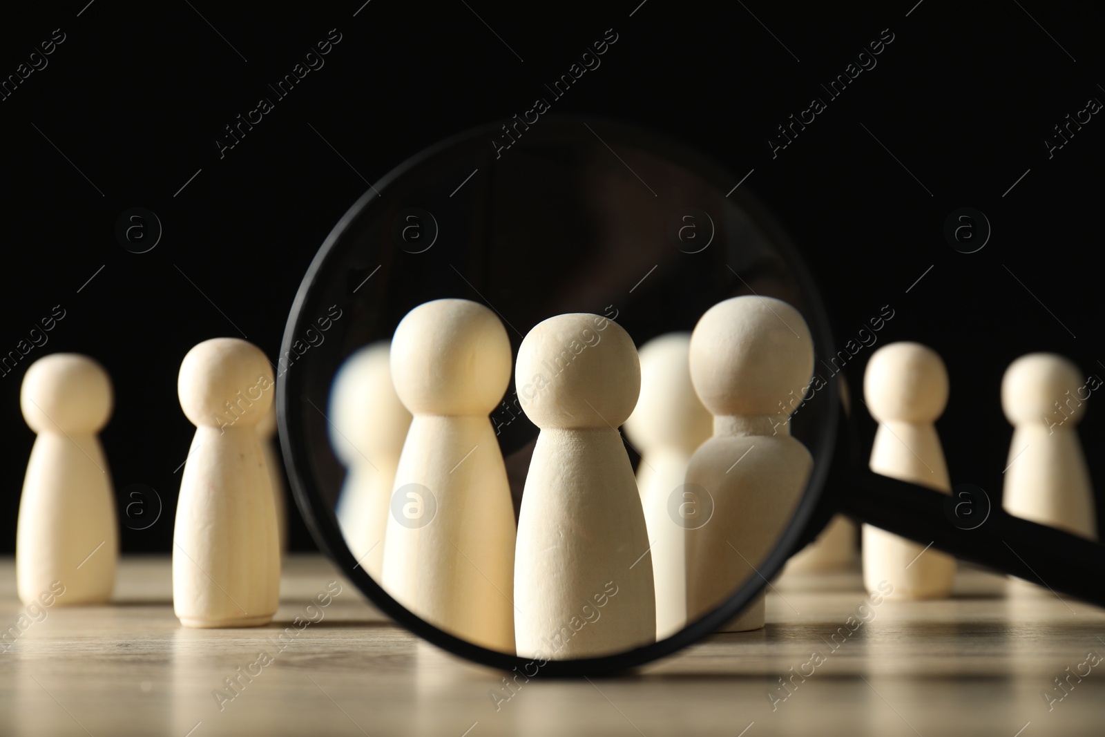 Photo of Human resources concept. Looking at wooden figures through magnifying glass on table against dark background, closeup