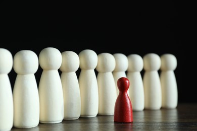 Photo of Human resources concept. Red figure in front of wooden ones on table against dark background, closeup