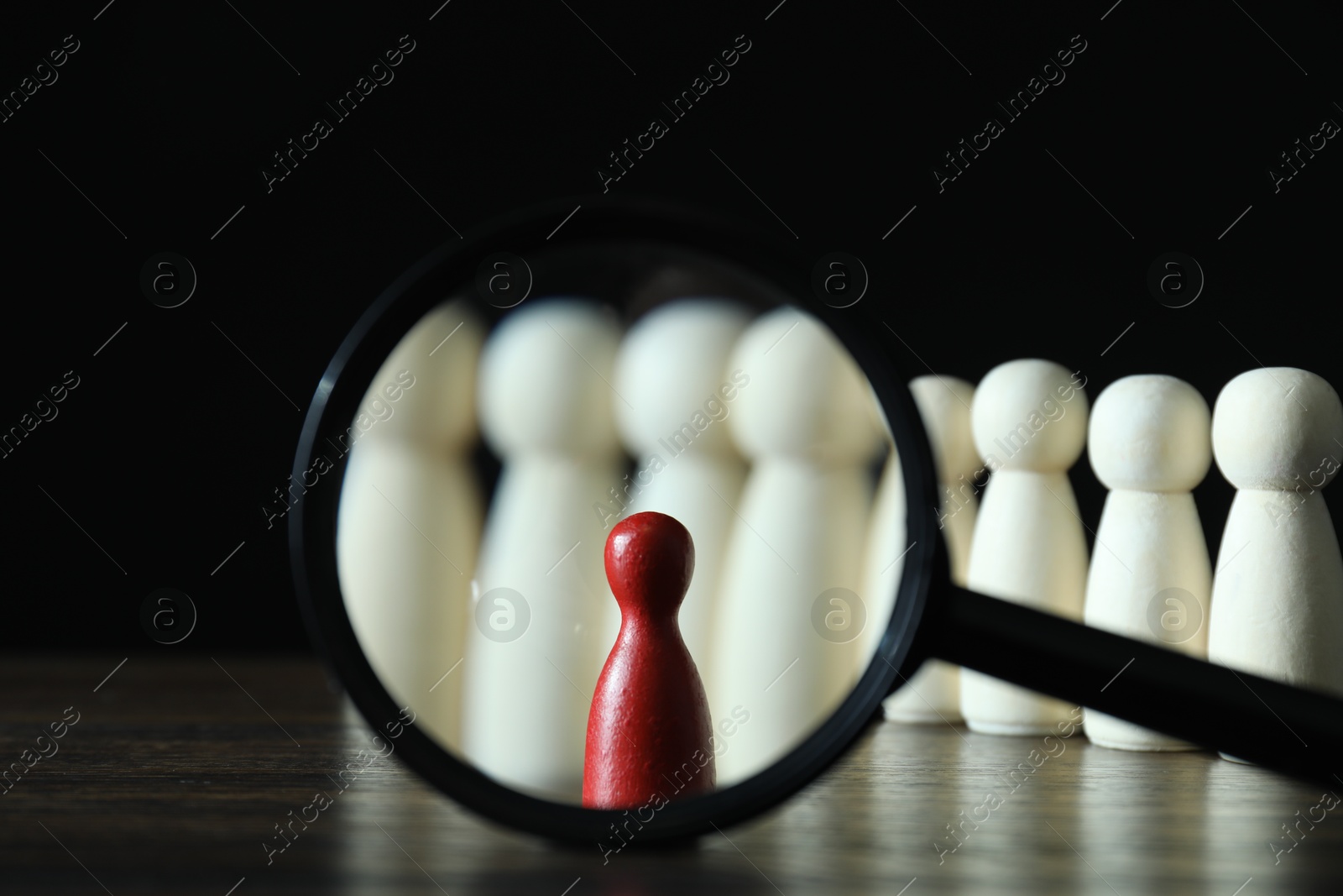 Photo of Human resources concept. Looking at red figure through magnifying glass on table against dark background, closeup