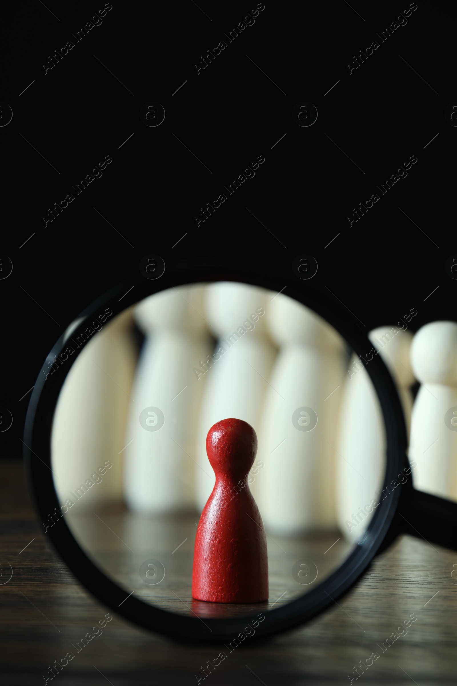 Photo of Human resources concept. Looking at red figure through magnifying glass on table against dark background, closeup