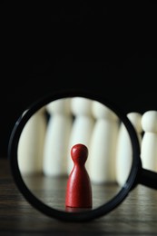 Photo of Human resources concept. Looking at red figure through magnifying glass on table against dark background, closeup