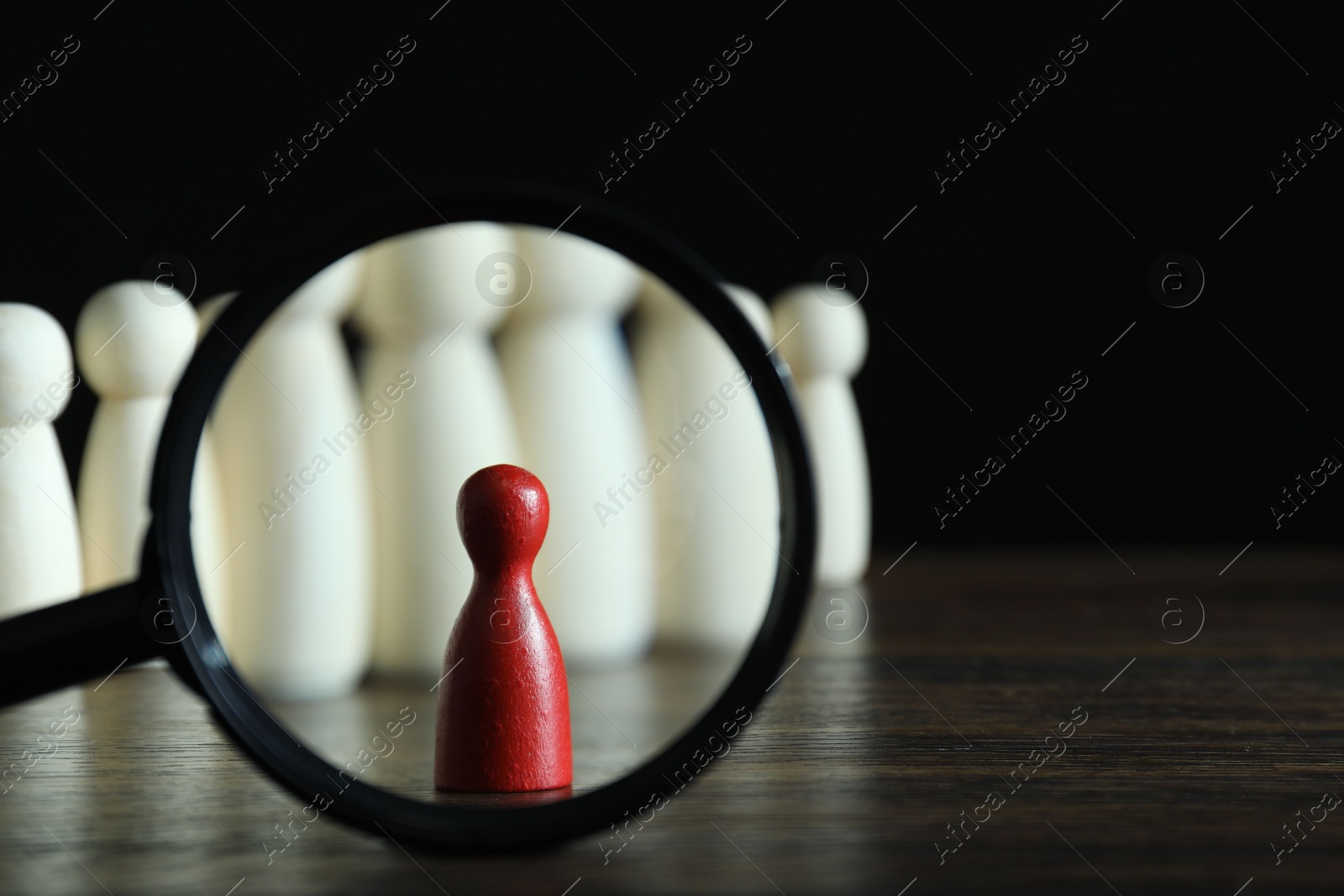 Photo of Human resources concept. Looking at red figure through magnifying glass on table against dark background, closeup