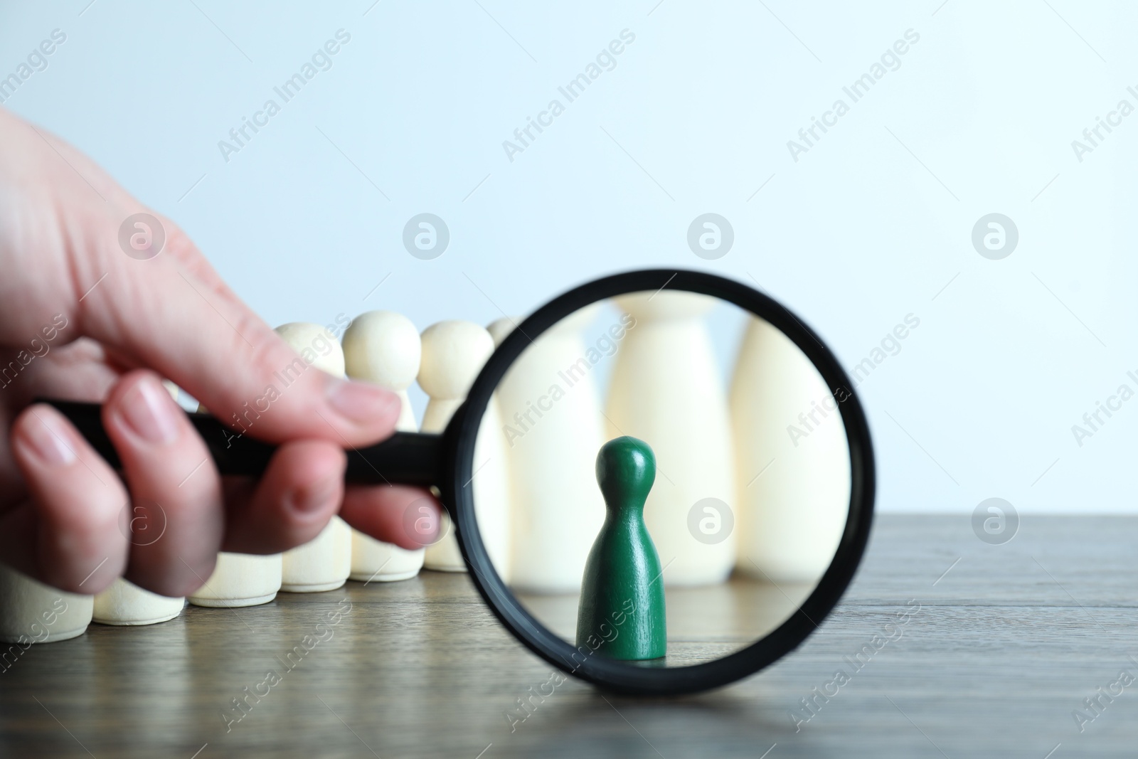 Photo of Human resources concept. Woman with magnifying glass and wooden pieces at table, closeup