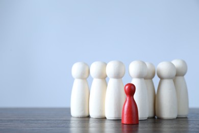 Photo of Human resources concept. Red figure among wooden ones on table against light background, closeup. Space for text