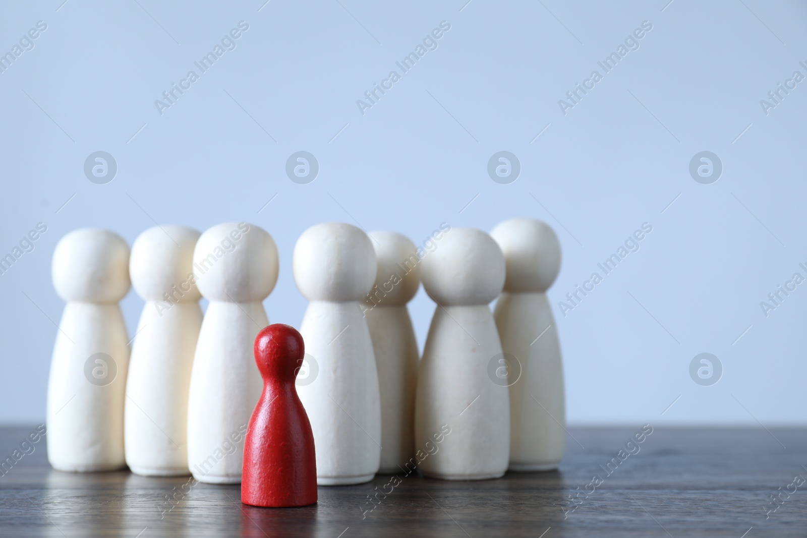 Photo of Human resources concept. Red figure among wooden ones on table against light background, closeup