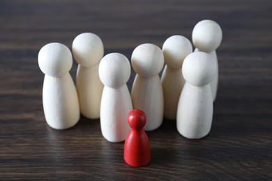 Photo of Human resources concept. Red figure among wooden ones on table, closeup