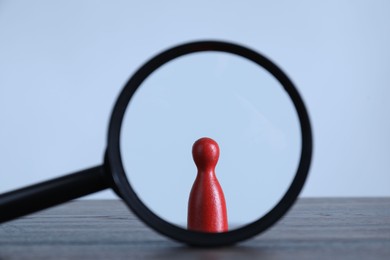 Photo of Human resources concept. Looking at red figure through magnifying glass on table against light background, closeup