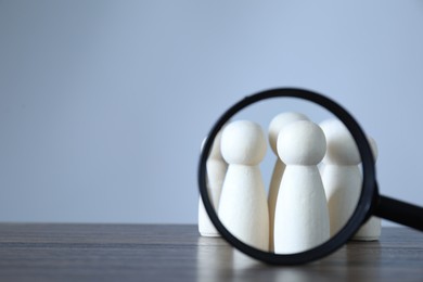 Photo of Human resources concept. Looking at wooden figures through magnifying glass on table against light background, closeup. Space for text